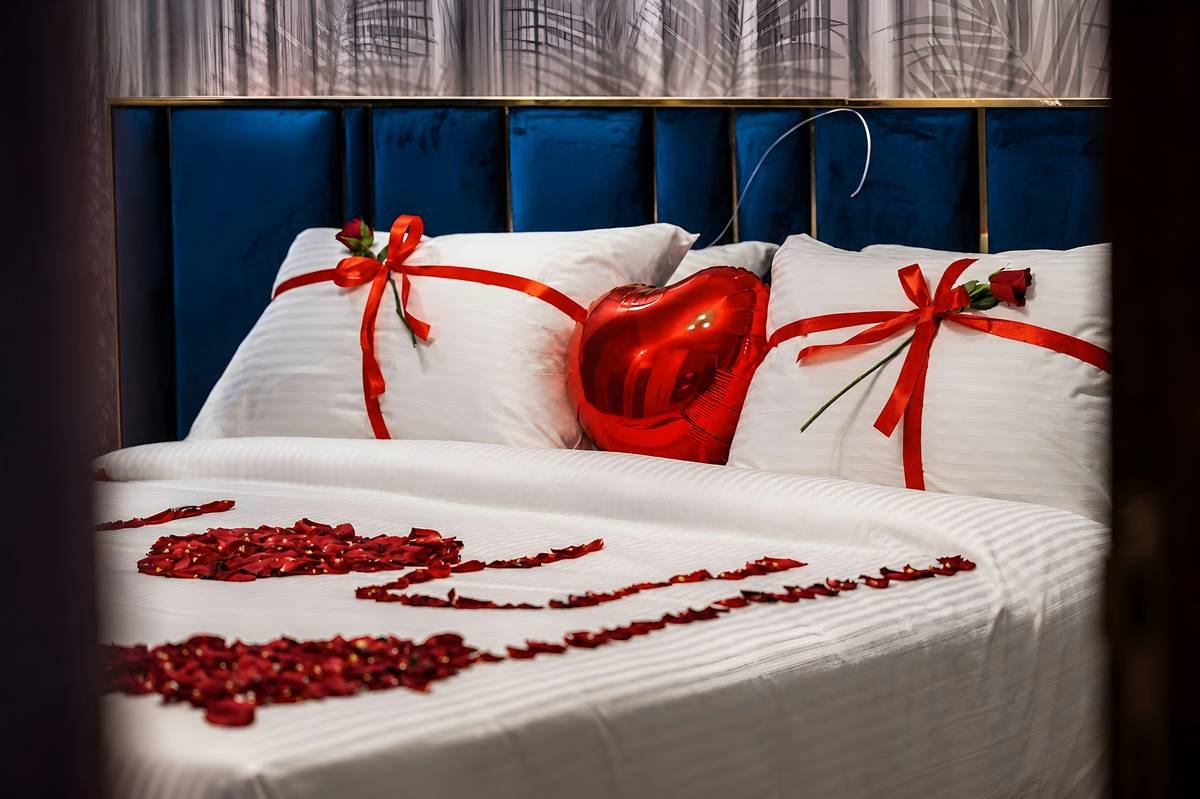 happy anniversary design in room featuring soft string lights, framed photos, rose petals on a bed, and a handwritten note on a nightstand